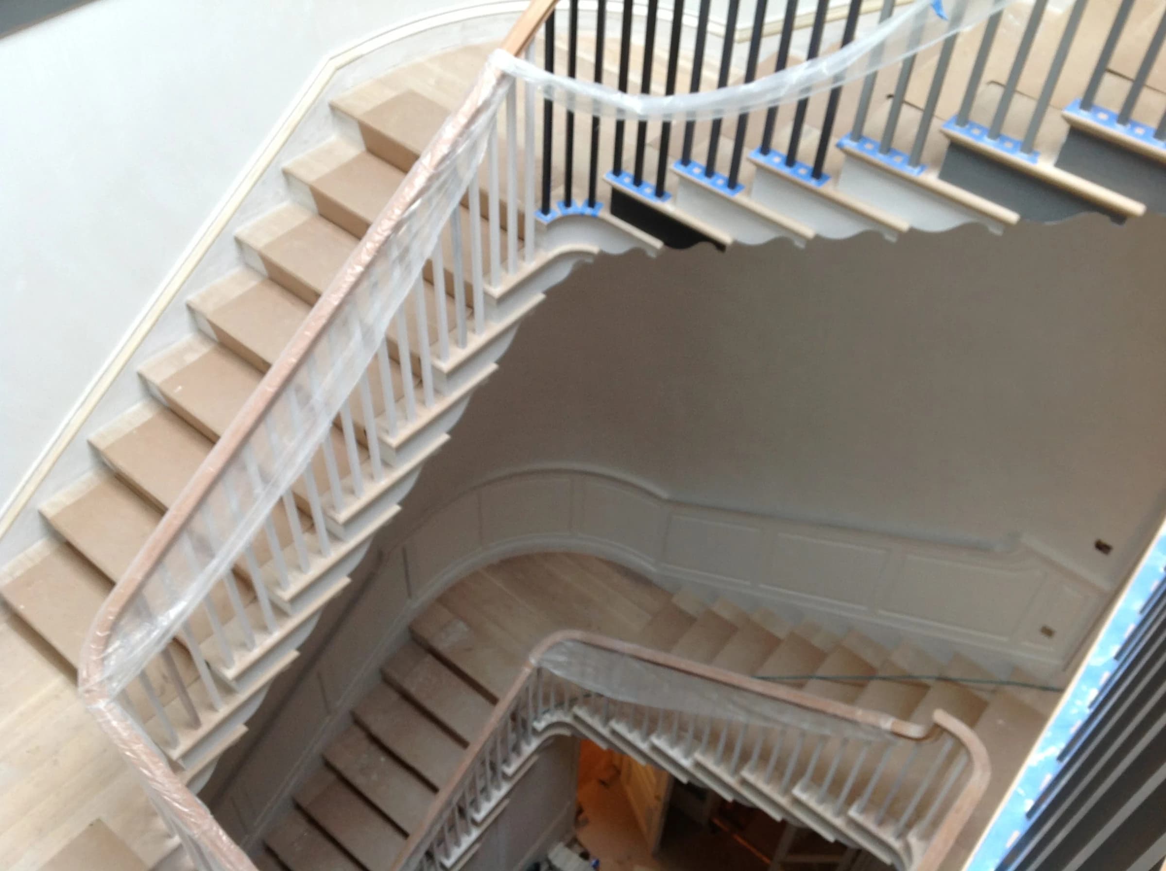 The same stairwell during work, with protective wrapping and unfinished-looking pale treads, photographed from another angle.